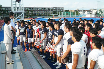 Football team members listening to President Tanaka’s pep talk