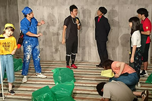 劇中の様子（”田町工科大学スーパー戦隊研究会”（写真左）とのエコロジー・ウォーに敗れる”法政大学ボランティアサークル”（写真右））